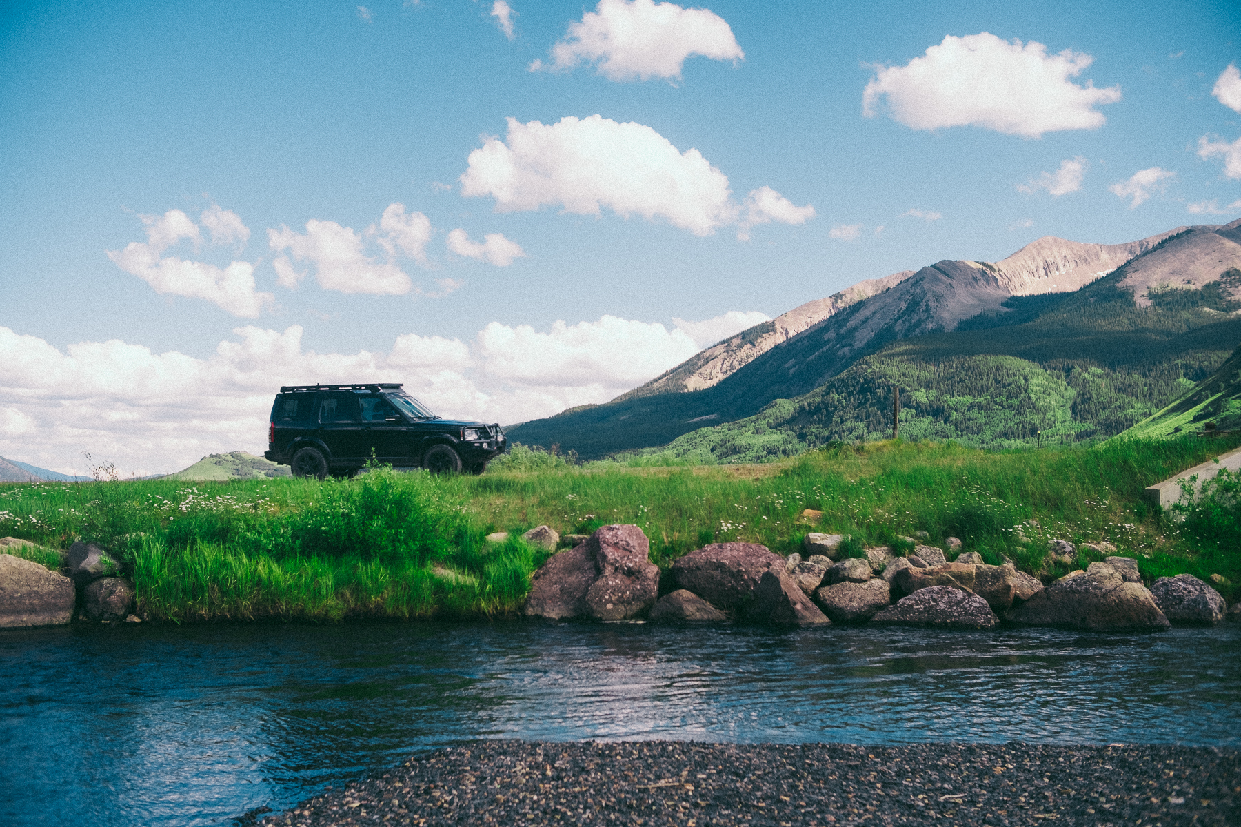 Off-road vehicle parked by a mountain stream on a sunny day